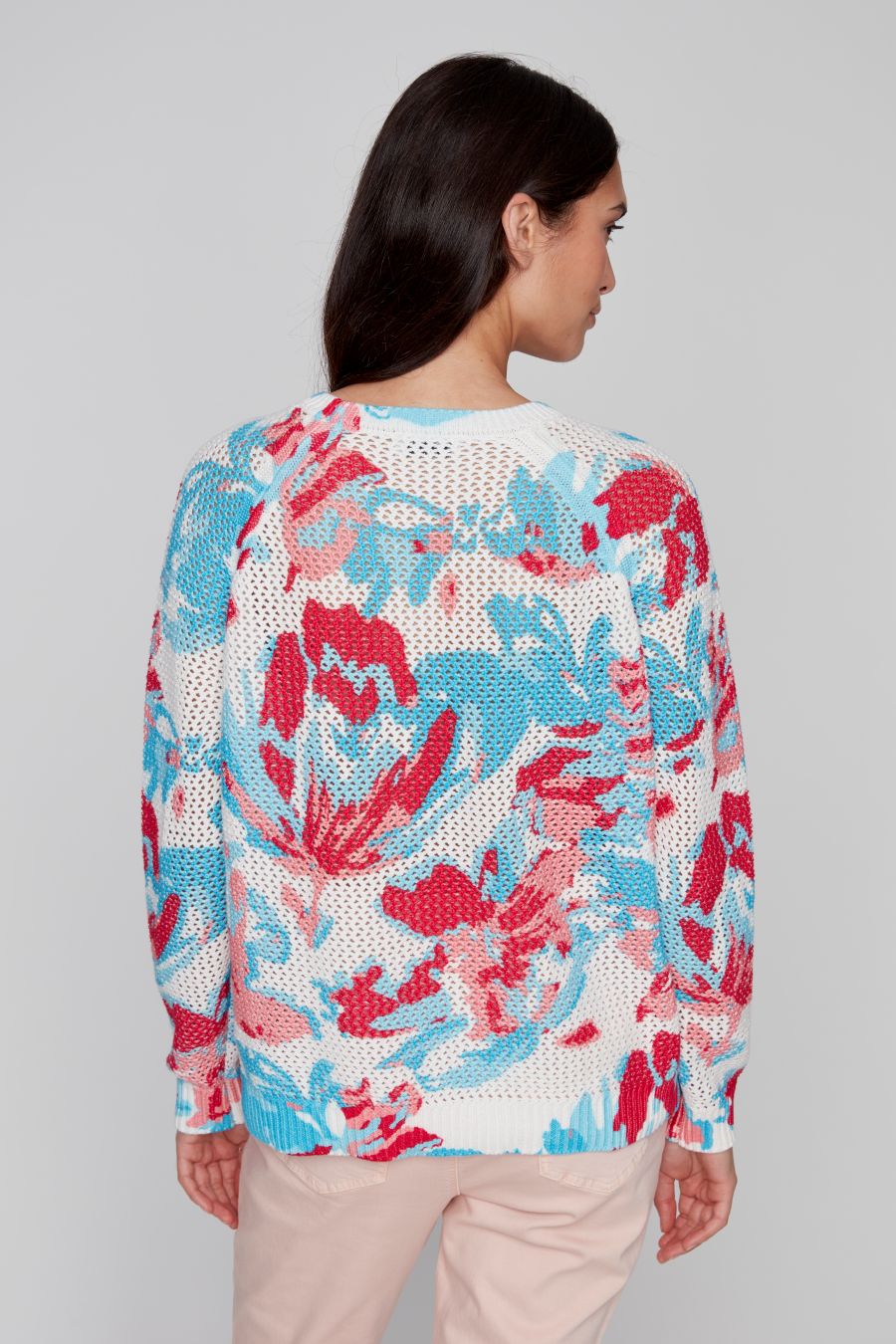 Back view of the open-knit long sleeve sweater in red, blue, and white on a model with long dark hair.