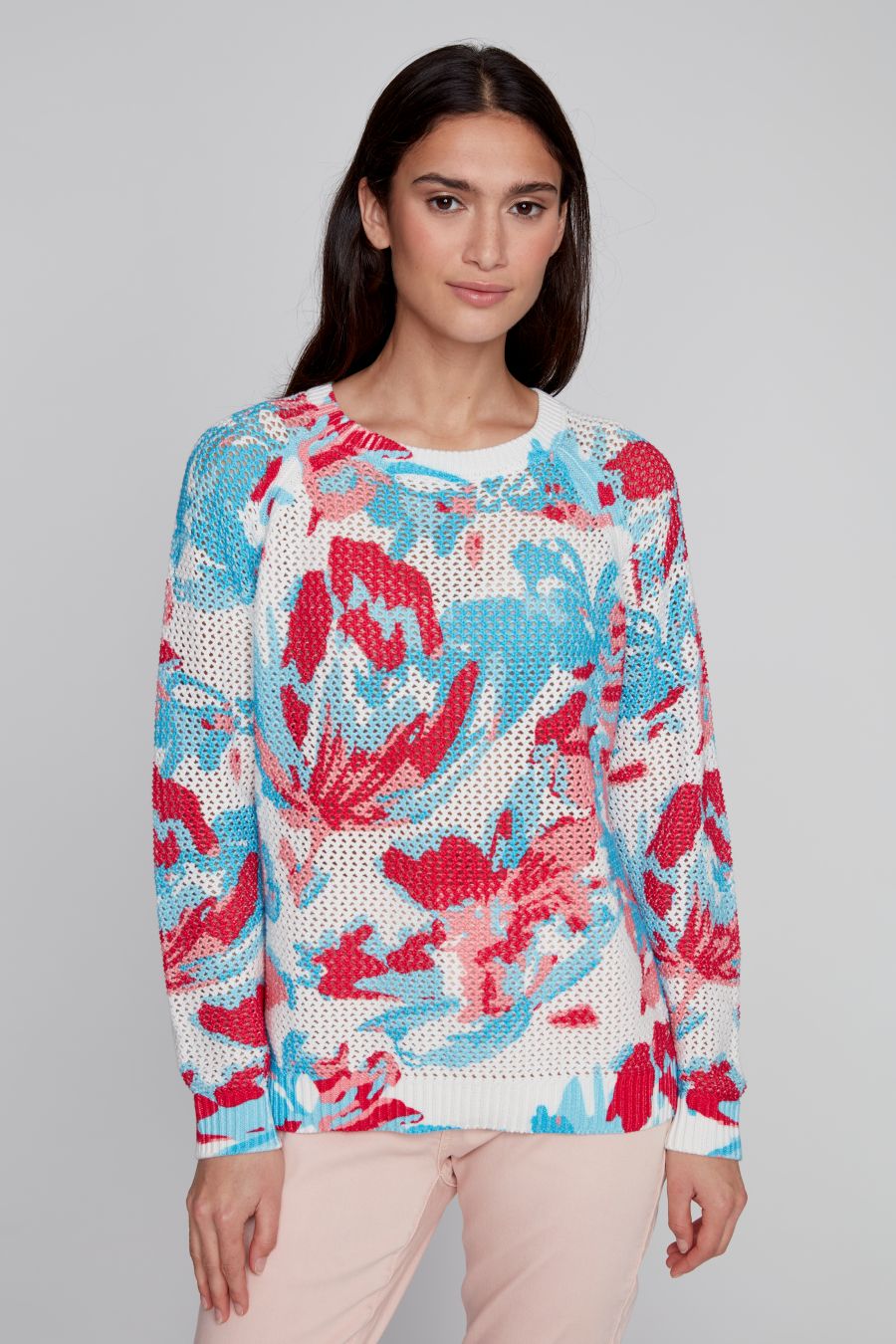 Front view of model wearing a white open-knit sweater with a red and blue floral silk-screen design by CYC.