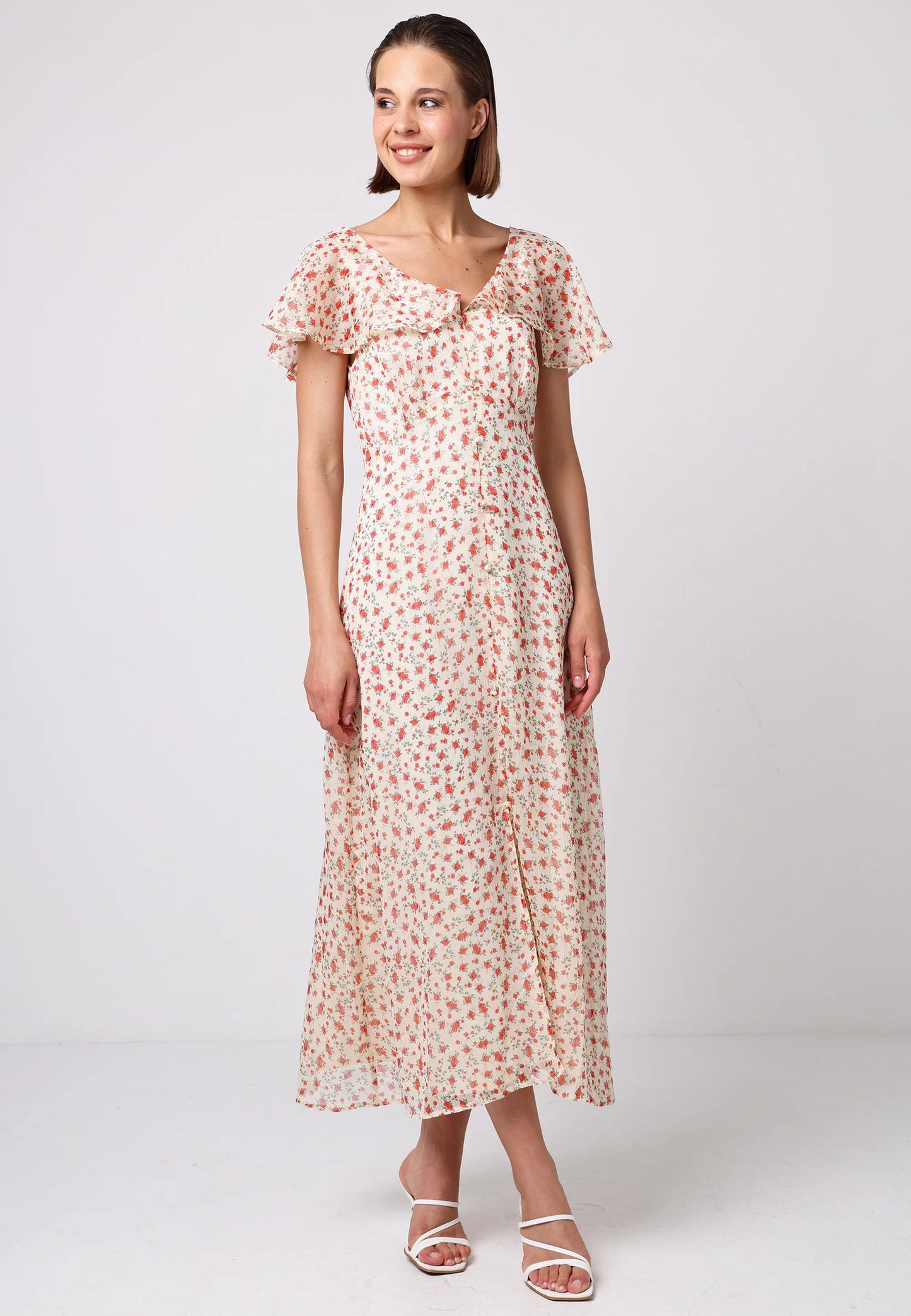 Model wearing romantic midi dress with red floral print, flutter sleeves, and front slit. Styled with white strappy heels on a neutral backdrop.