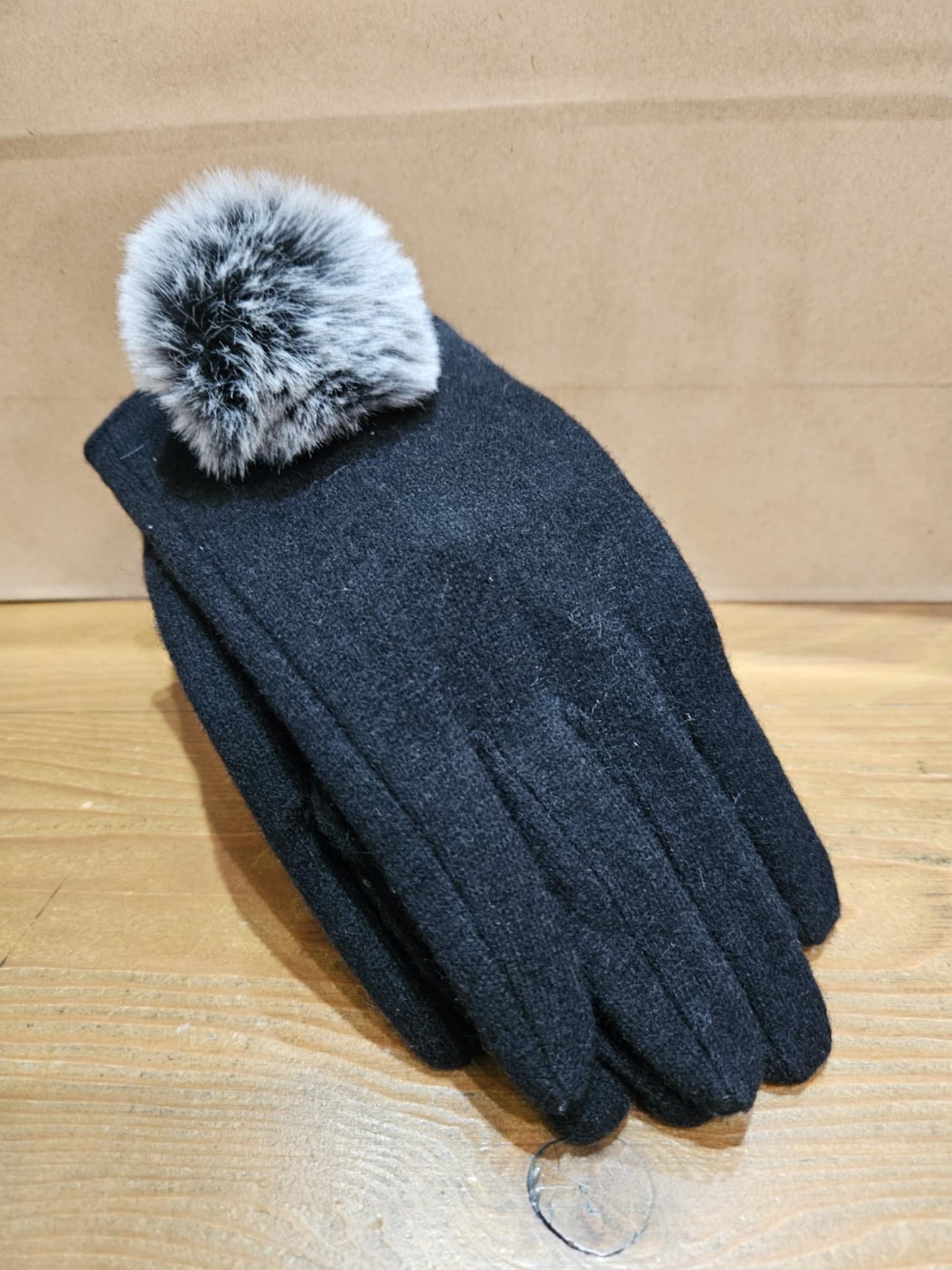 Single Morgan & Taylor Antonella Glove in black with a fluffy grey pom-pom, displayed on a wooden surface.