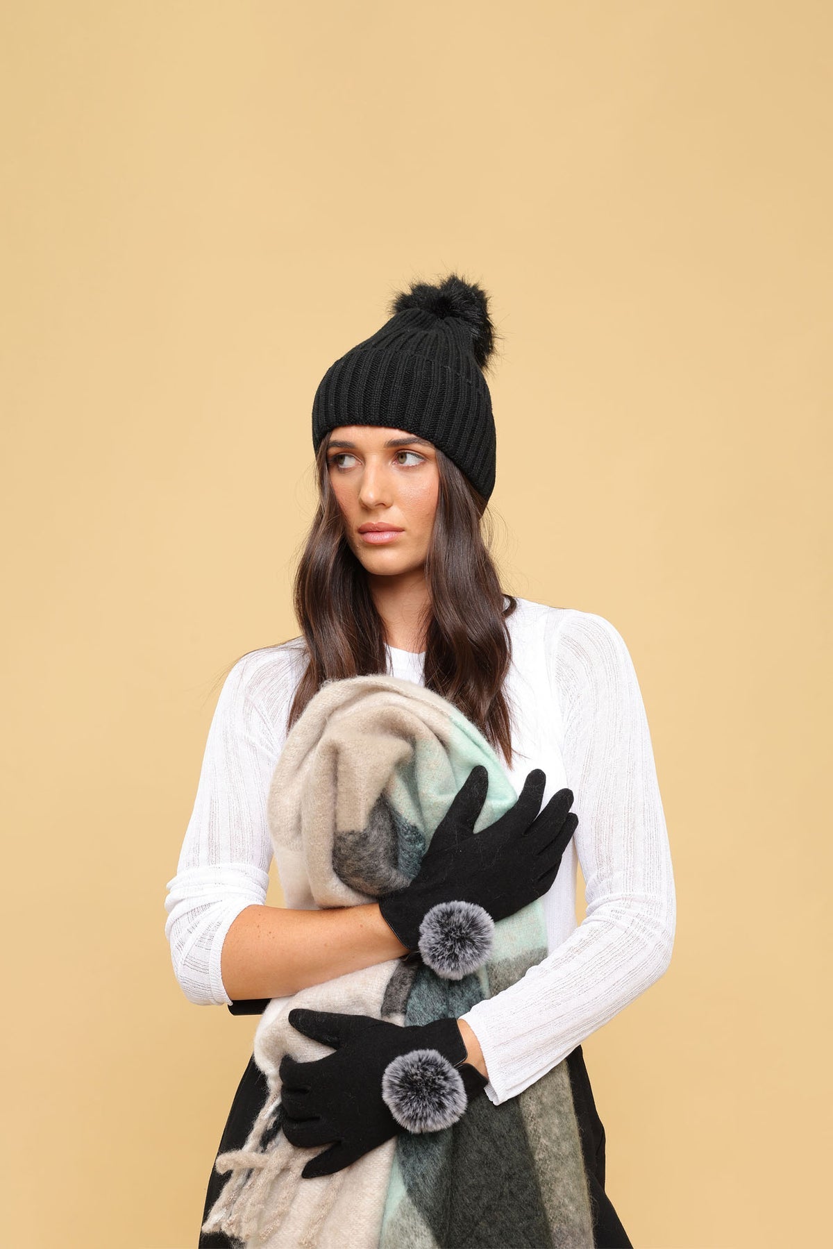 Model styled in Morgan & Taylor Antonella Gloves and a matching black beanie, holding a grey scarf against a neutral beige background.