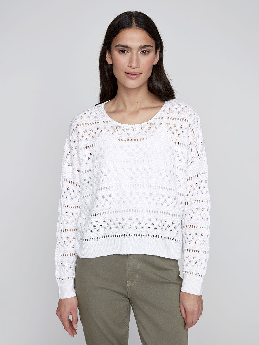 Model wearing a white waist-length long sleeve open-knit sweater with a diamond pattern