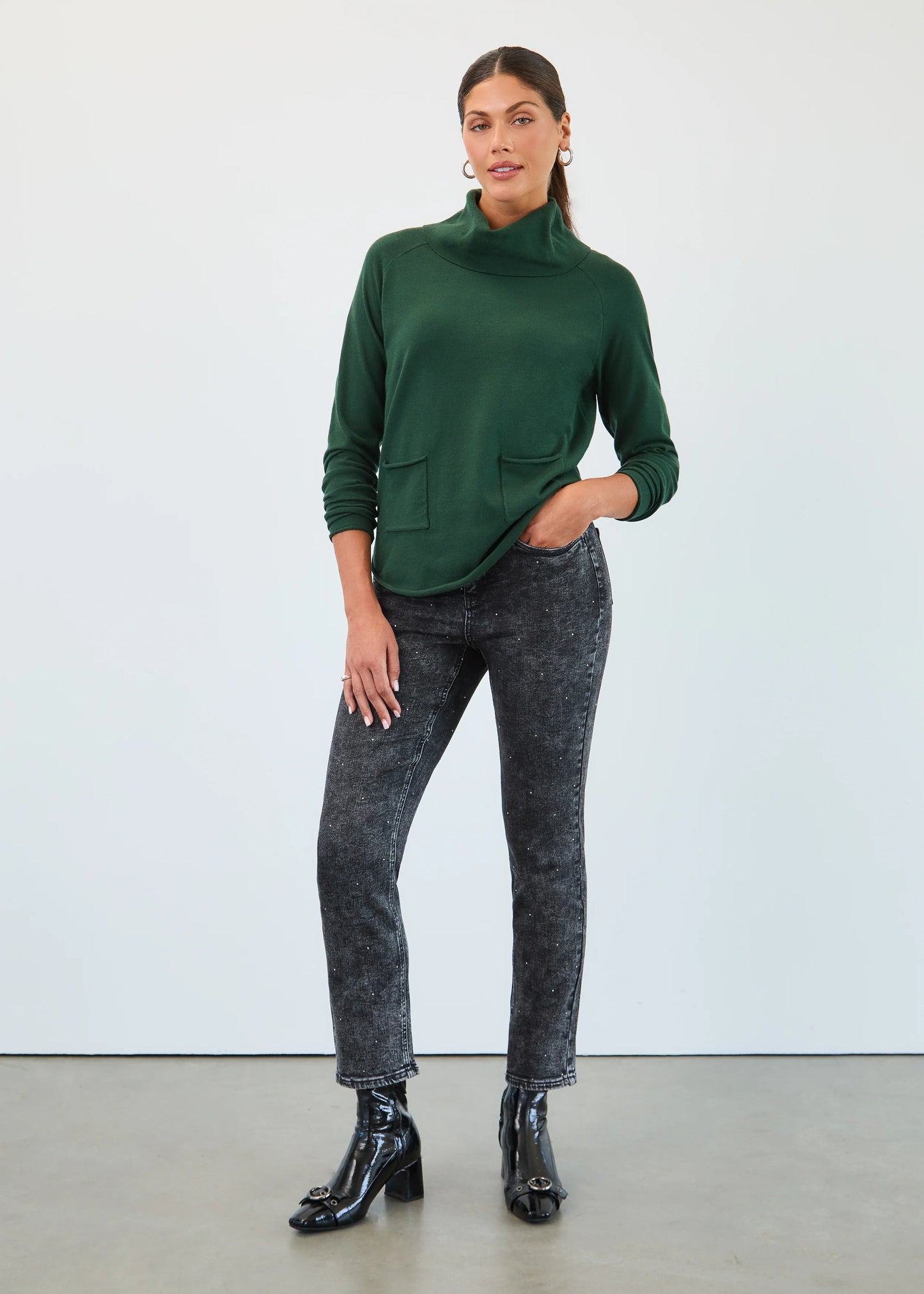 Woman wearing a FDJ's green cowl neck sweater and black acid-wash jeans against a white background.