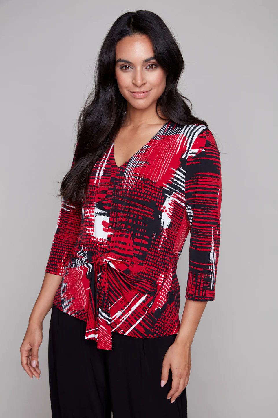 Woman wearing Compli K red, black, and white patterned V-neck top with tie-front and three-quarter sleeves.