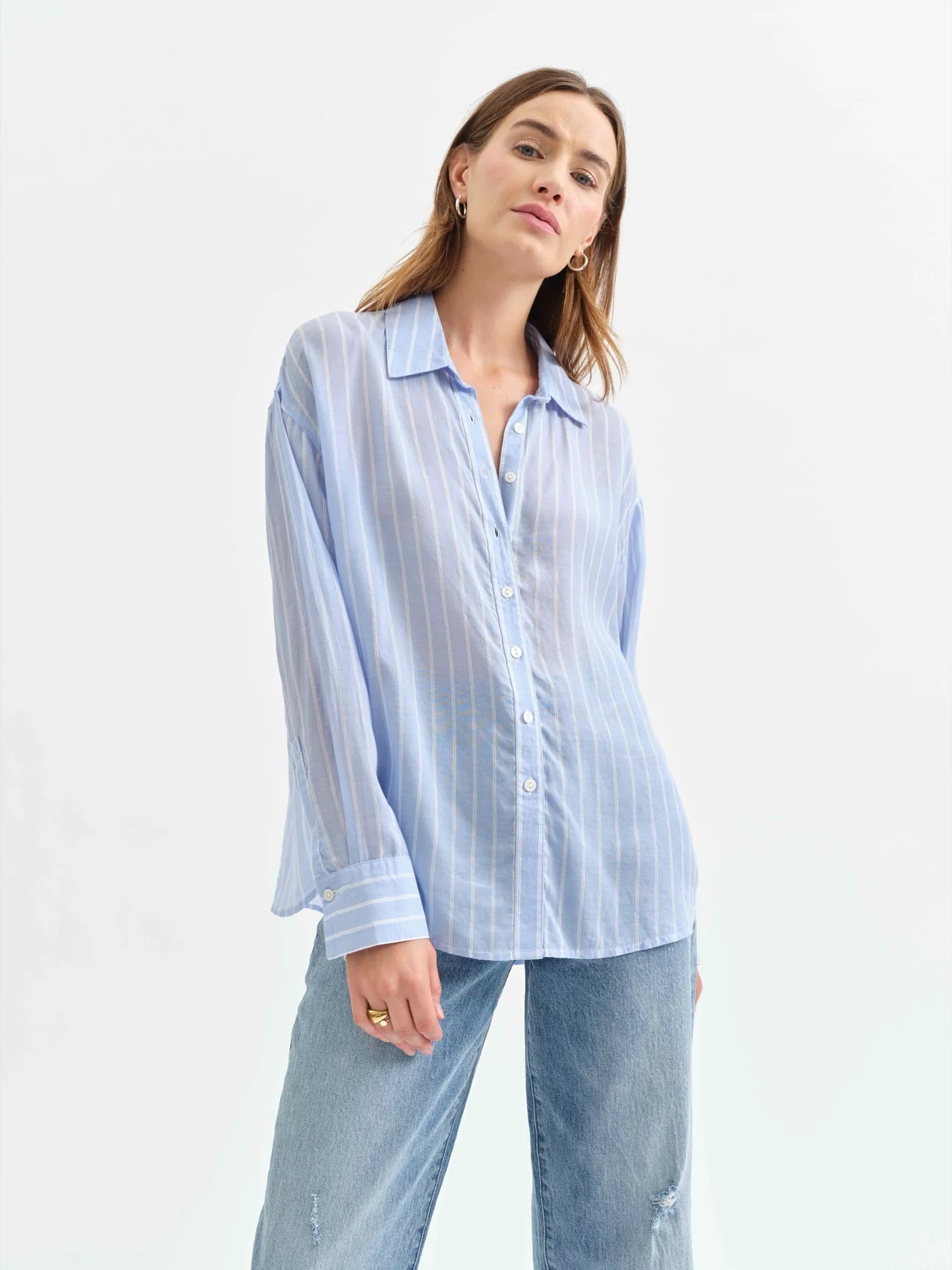 Model wearing the Daze Lotus Back Tie Long Sleeve Shirt in Castle Stripe. A classic blue and white striped button-up with a relaxed fit and menswear-inspired design, styled with light-wash denim jeans.