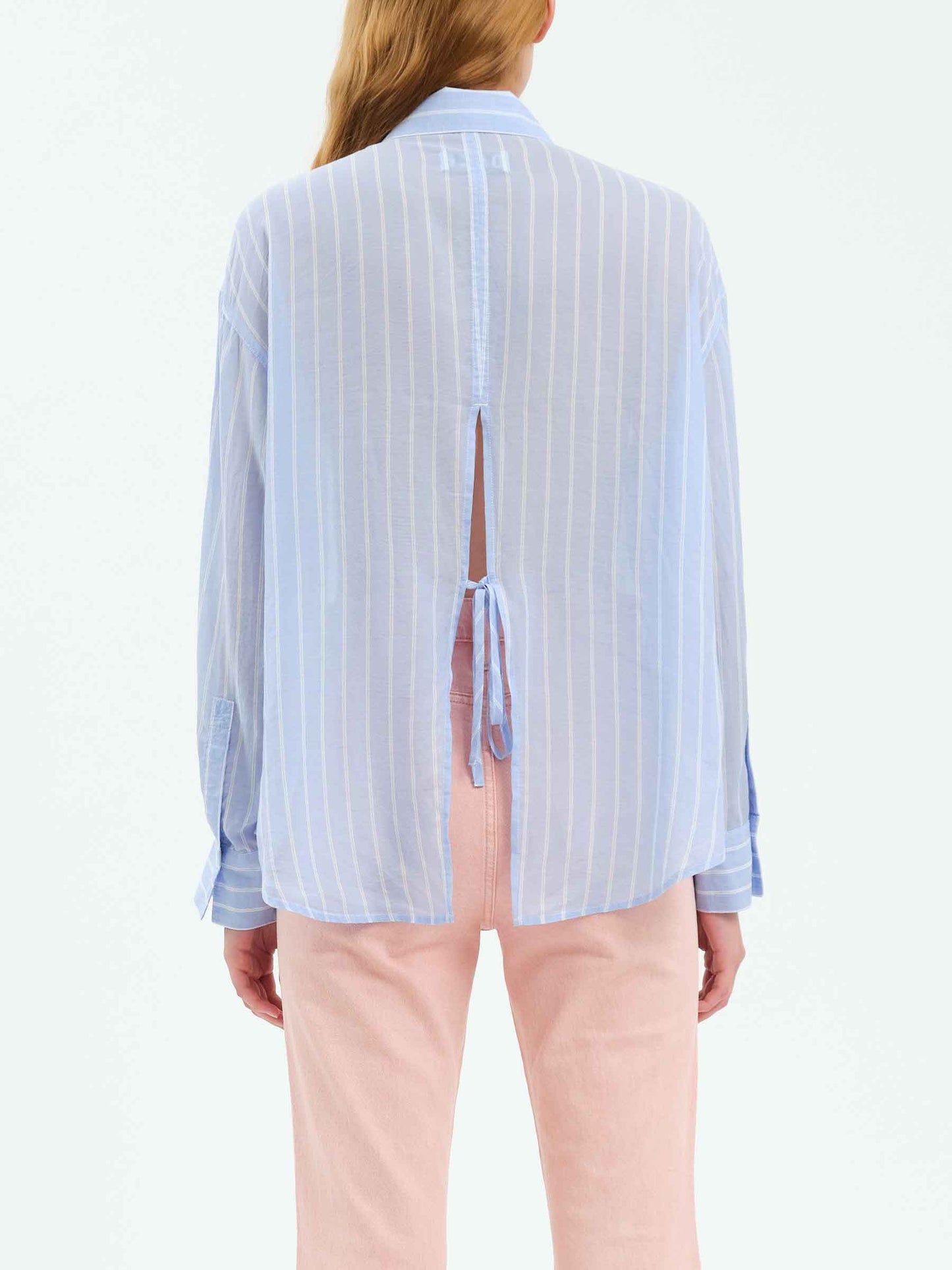 Full back view of the Daze Lotus Back Tie Long Sleeve Shirt, styled with pink trousers, clearly displaying the open-back cut and back-tie closure for adjustable styling.