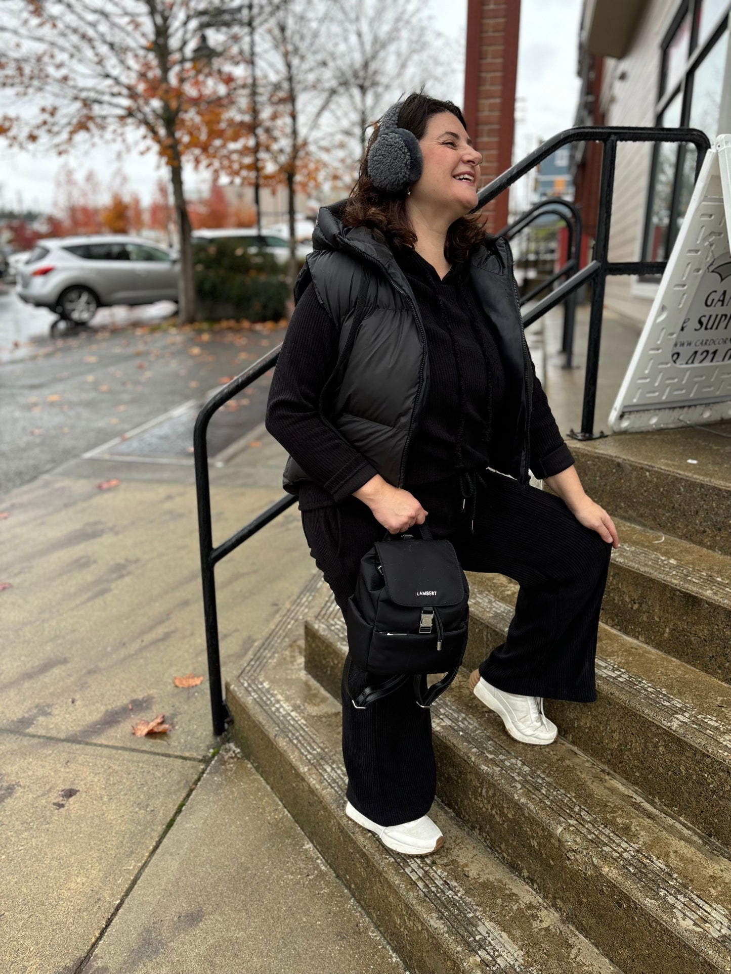 Model wearing black C.C Beanie Faux Fur Sherpa Earmuffs outdoors, styled with a black puffer vest for a cozy winter look.