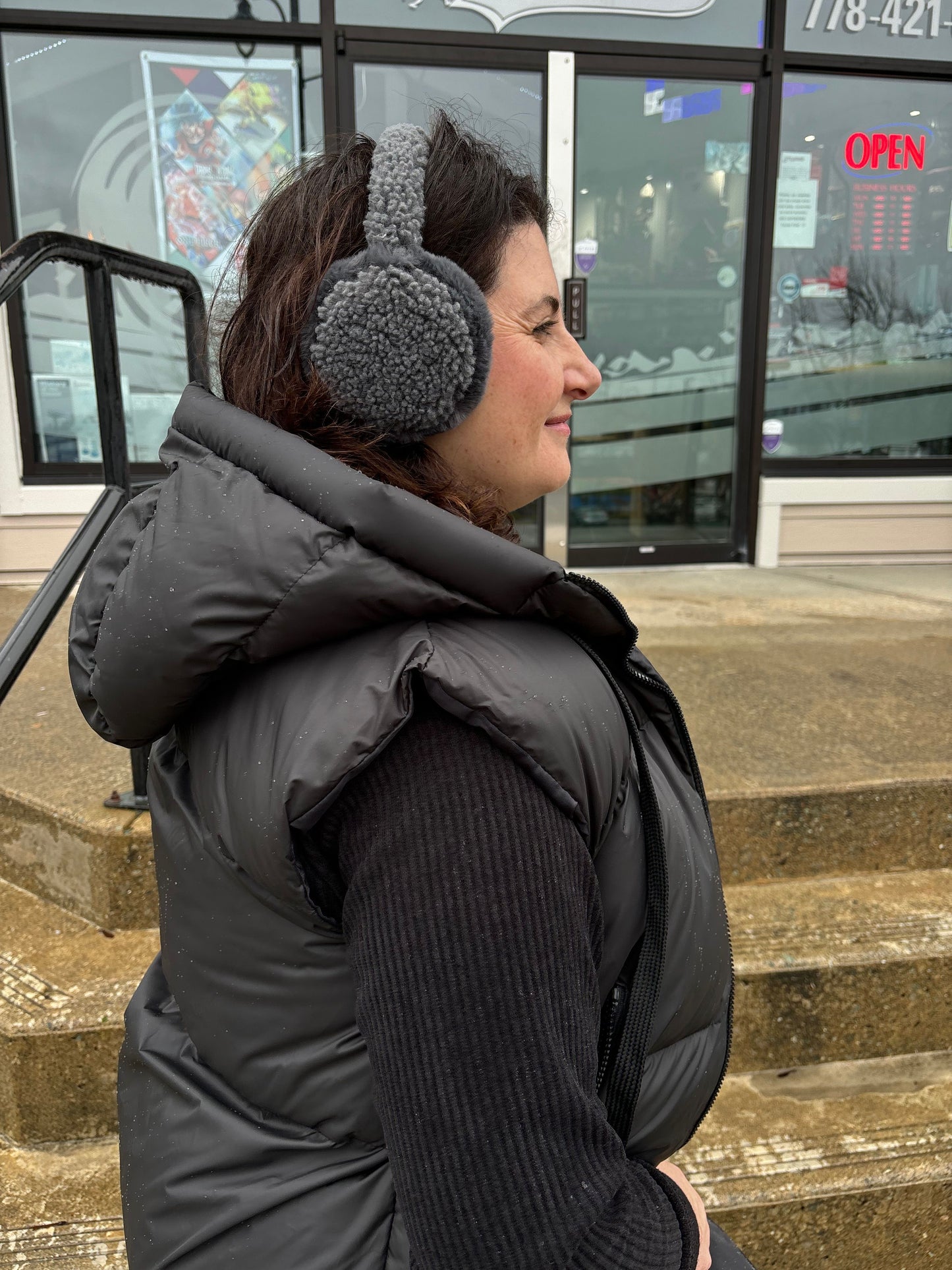 Close-up, side view of a woman wearing grey C.C Beanie Faux Fur Sherpa Earmuffs, styled with a black winter coat for a comfortable and stylish cold-weather look