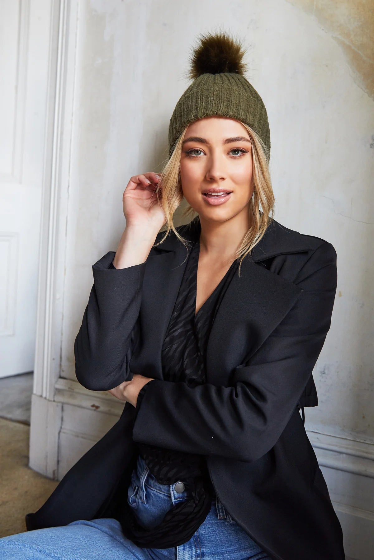 Model wearing the Morgan & Taylor Zara Beanie in olive green with a fluffy pom-pom, paired with a black blazer and jeans.