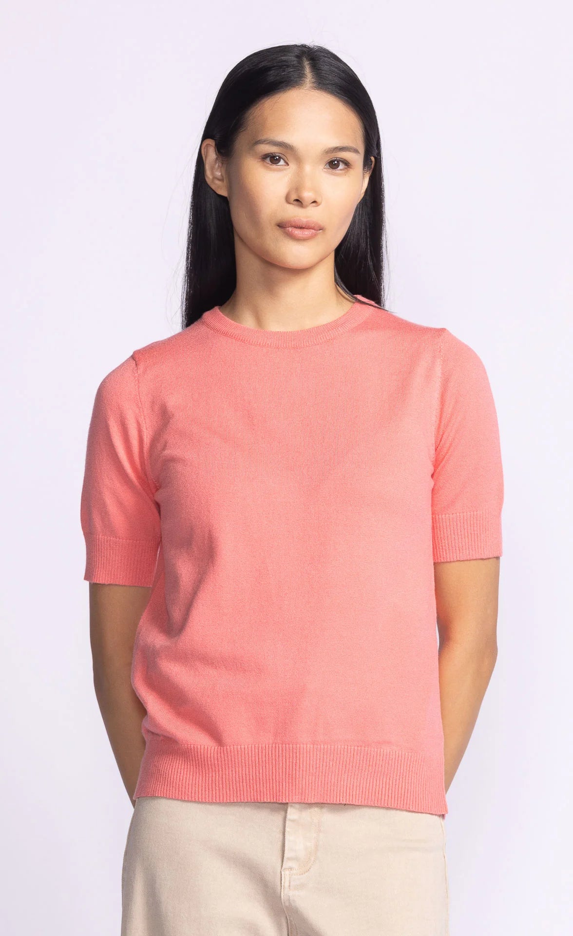 Model wearing Pink Martini's Sandy Top in coral, showcasing its relaxed fit and breathable knit fabric.