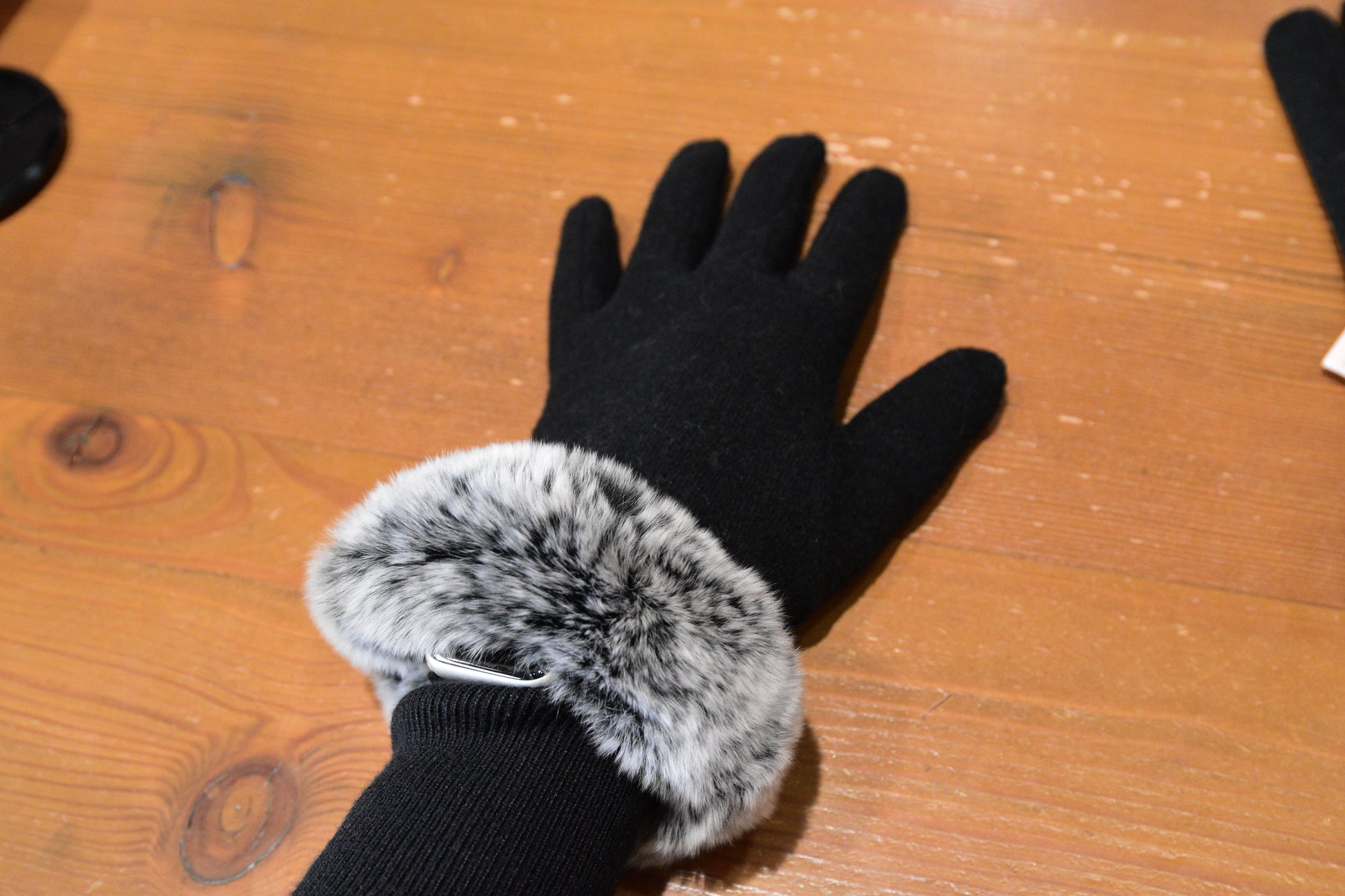 Model wearing one of Morgan & Taylor's Sally Gloves in black with fluffy grey faux fur cuffs, laid flat on a wooden surface.