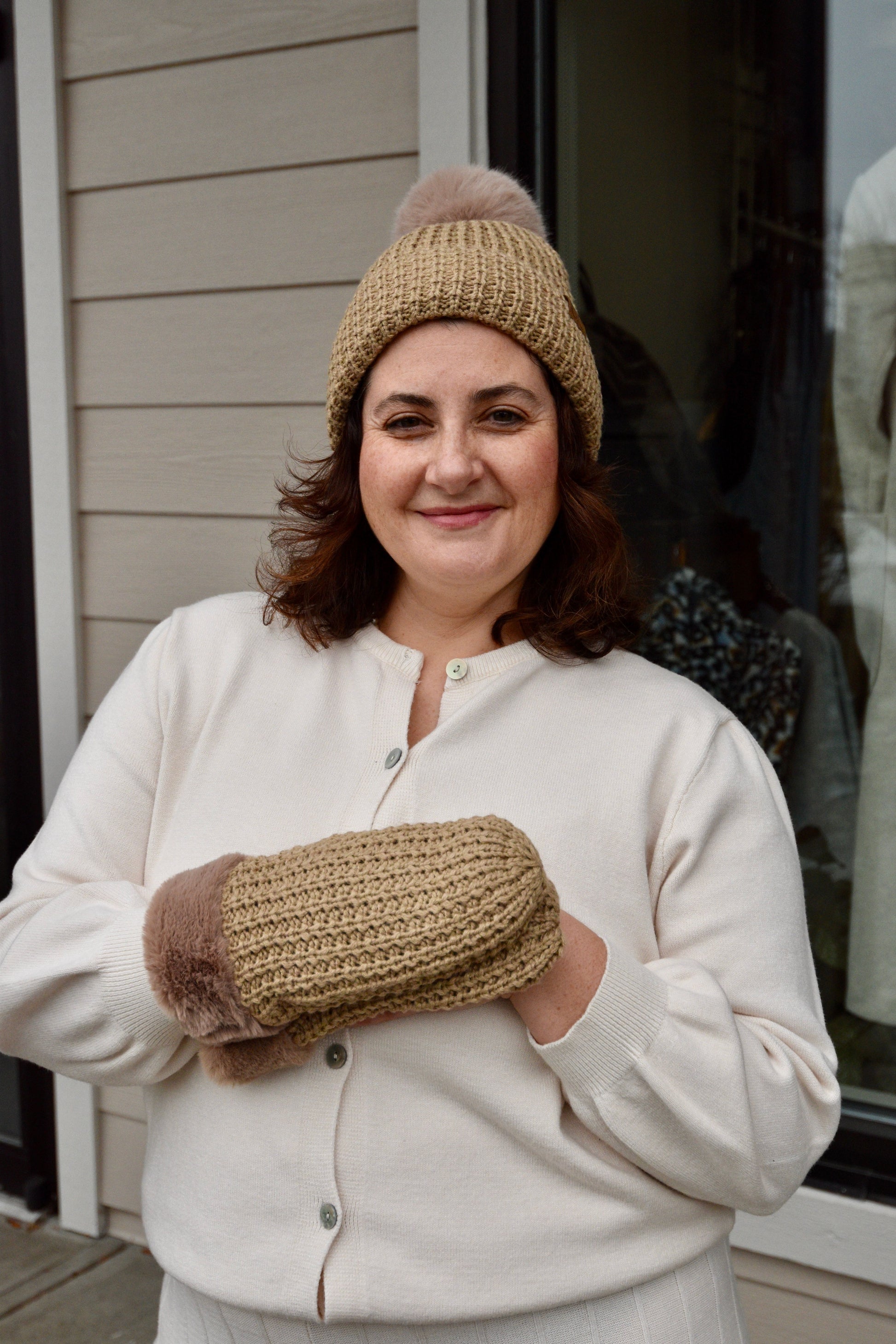 Woman wearing the tan C.C Waffle Knit Mittens and matching beanie, posing outdoors in a casual winter outfit.