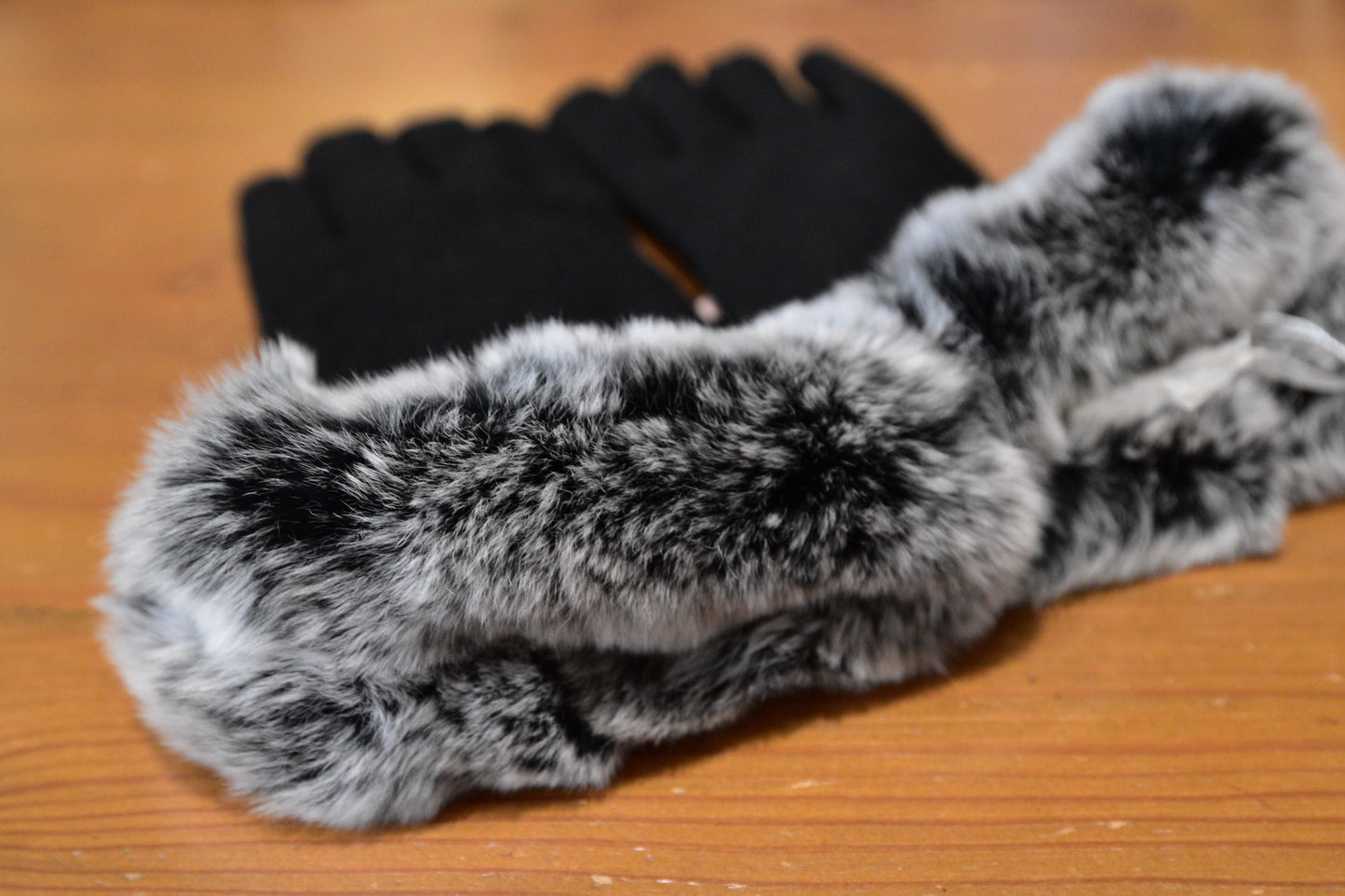 Morgan & Taylor Sally Gloves in black with fluffy grey faux fur cuffs, laid flat on a wooden surface with a product tag attached.