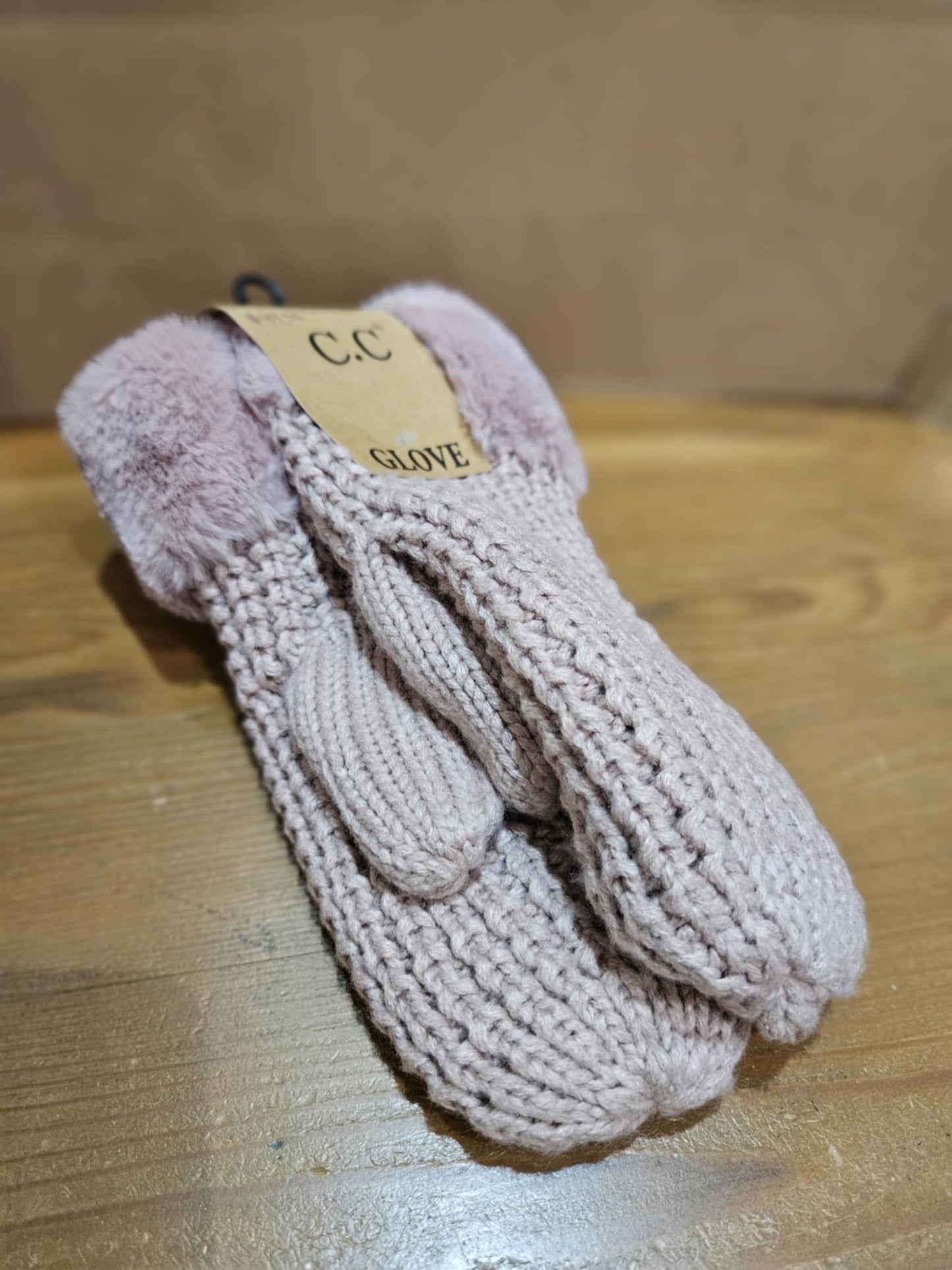 Flat lay of C.C Waffle Knit Mittens in dusty pink, highlighting their soft faux fur lining and textured waffle knit design on a wooden surface.