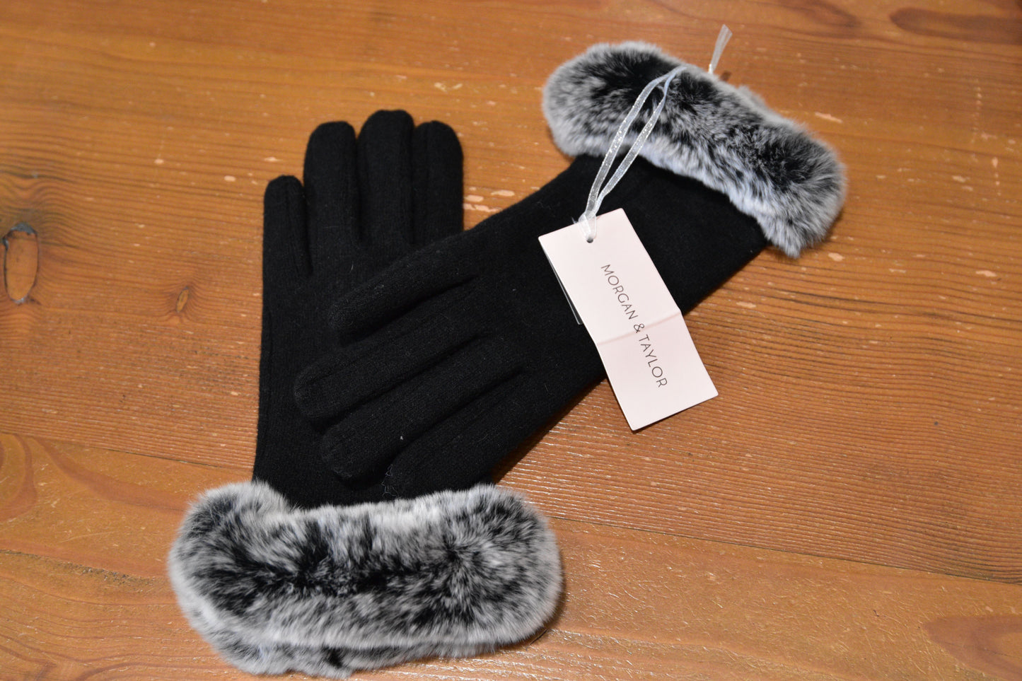 Side-by-side view of Morgan & Taylor Sally Gloves, showcasing their elegant faux fur cuffs and sleek black design, arranged on a warm wood table.