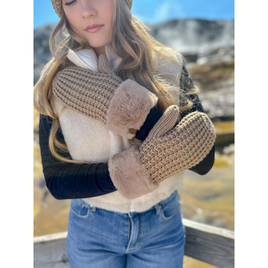 Model wearing tan C.C Waffle Knit Mittens with soft faux fur cuffs, paired with a beige fleece vest and jeans in a mountain setting.