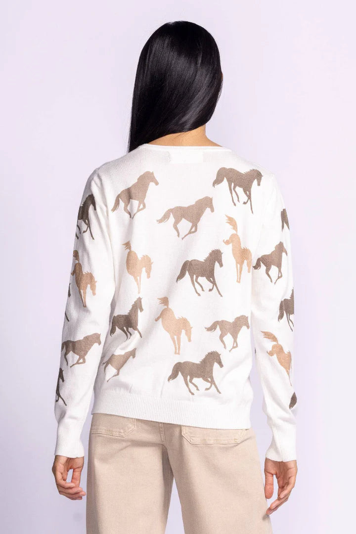 Back view of the Wild Horses sweater by Pink Martini, featuring a white knit design with a brown horse print pattern, worn by a model with long dark hair.