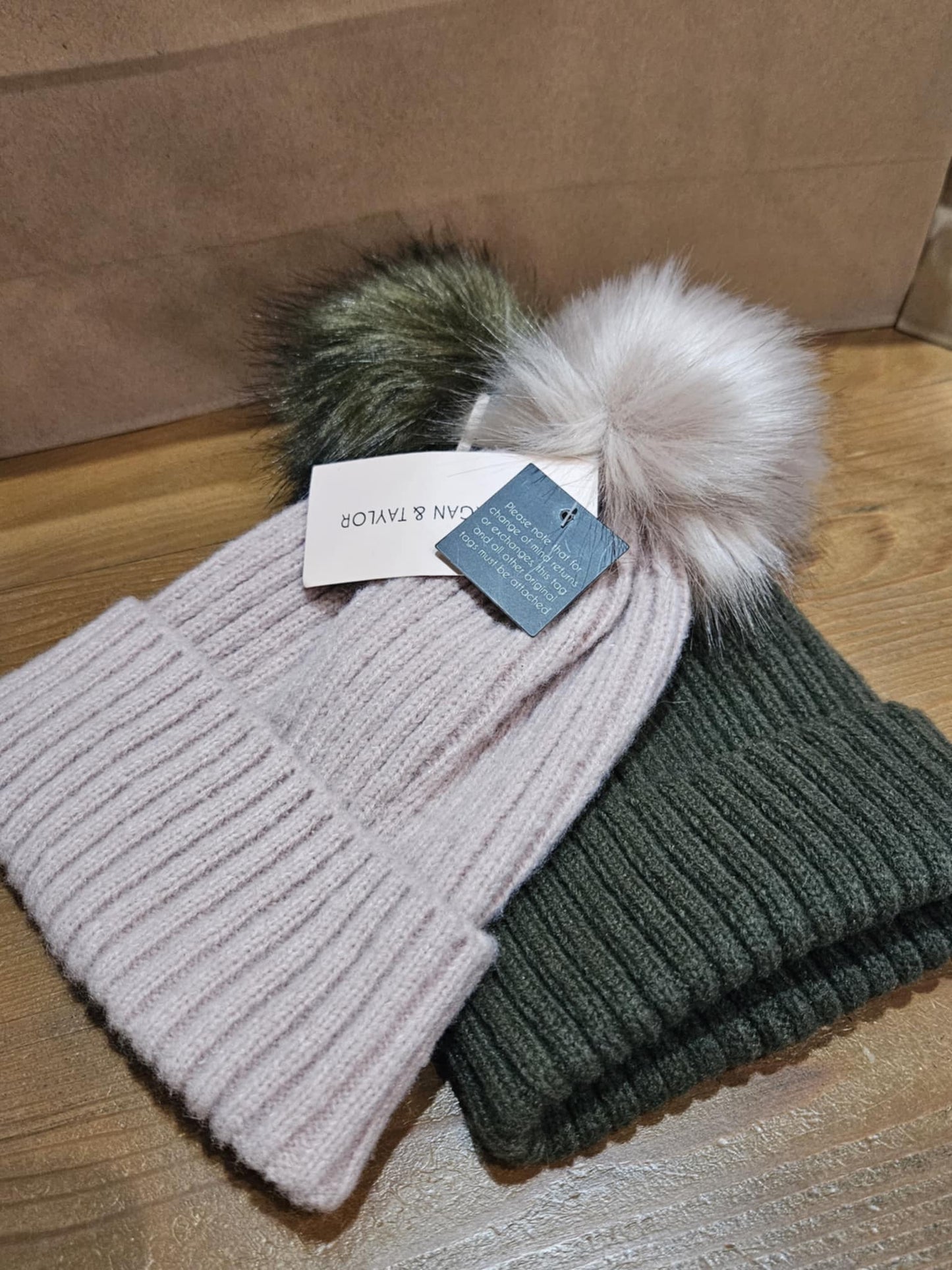 Close-up of an army green and pale pink Morgan & Taylor Zara Beanie with a faux fur pom-pom, displayed flat on a wooden surface.